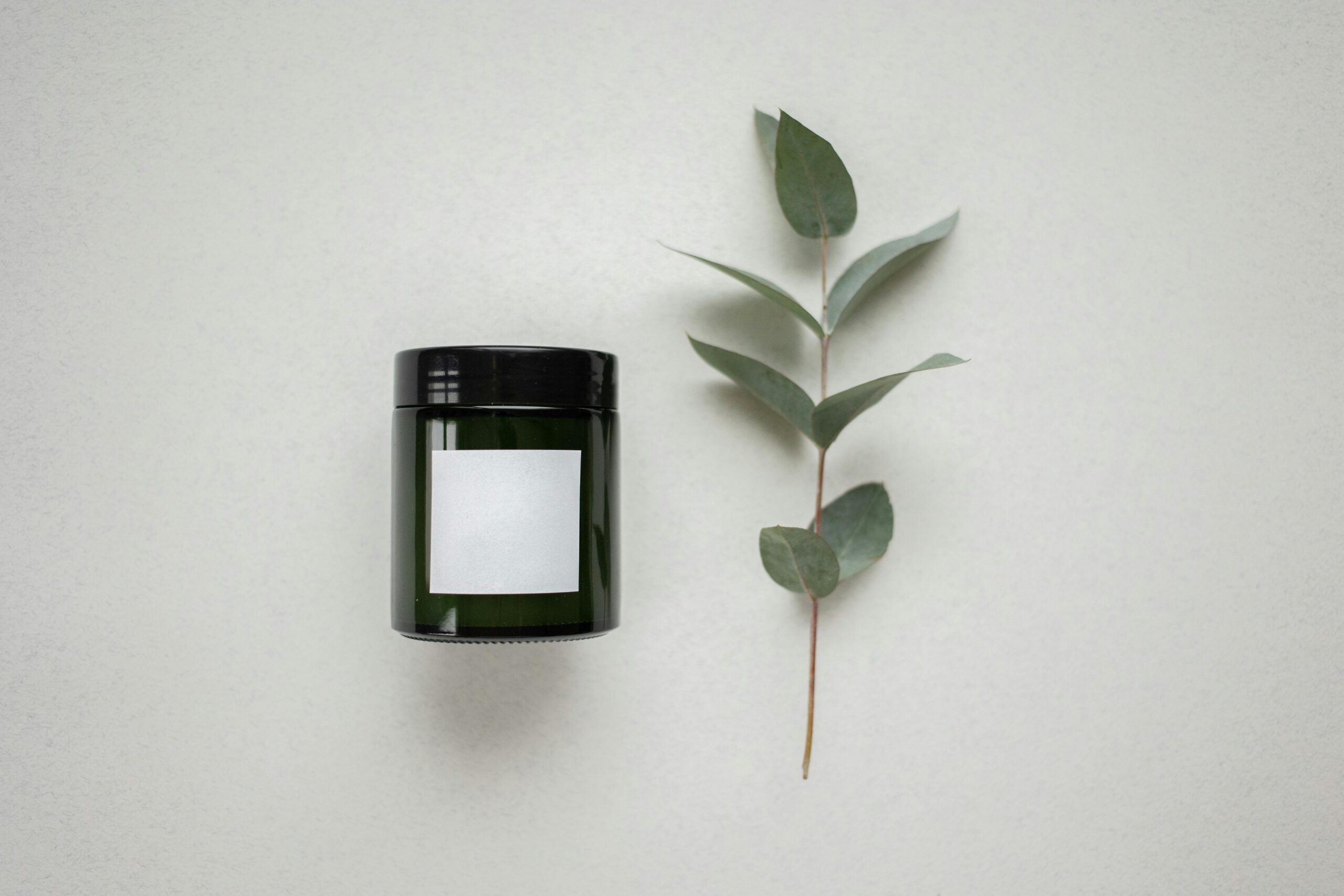 Elegant product mockup featuring a dark glass jar and eucalyptus on a white background.